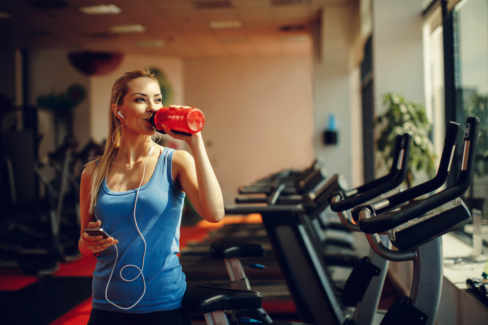 Beautiful young woman resting and drinking water in the gym