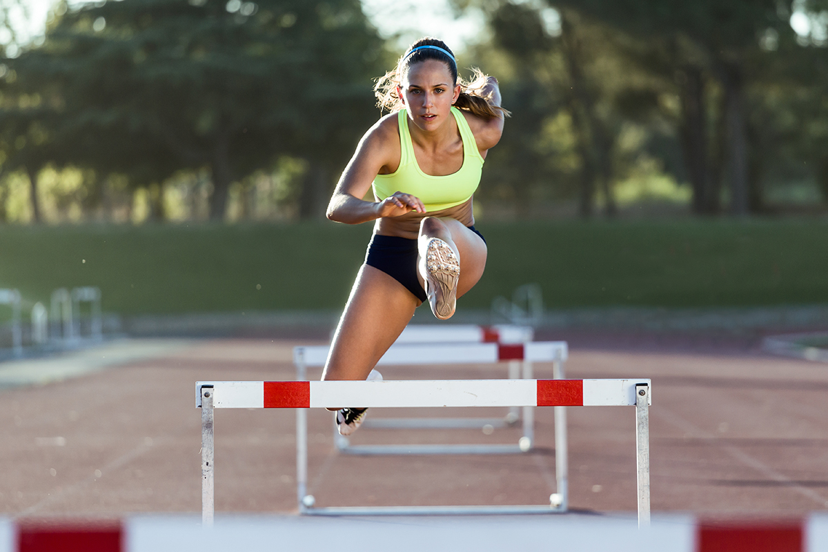 Portrait of young athlete jumping over a hurdle during training on race track.